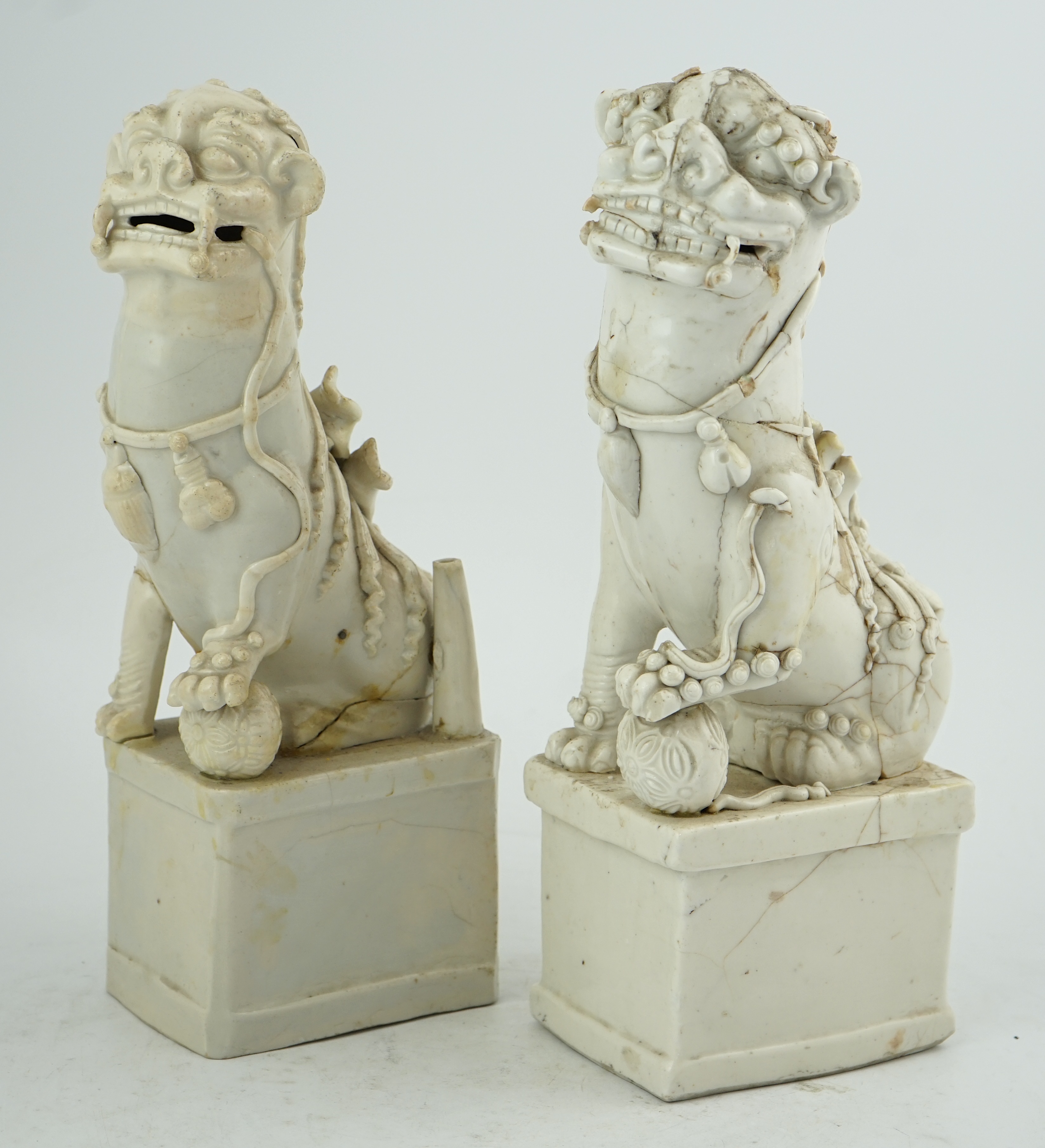 Two large Chinese Dehua blanc de chine Buddhist lion joss-stick holders, Kangxi period, each seated, one paw raised on a ball, on rectangular pedestal basis, 35cm high, Condition - extensive cracks or repairs